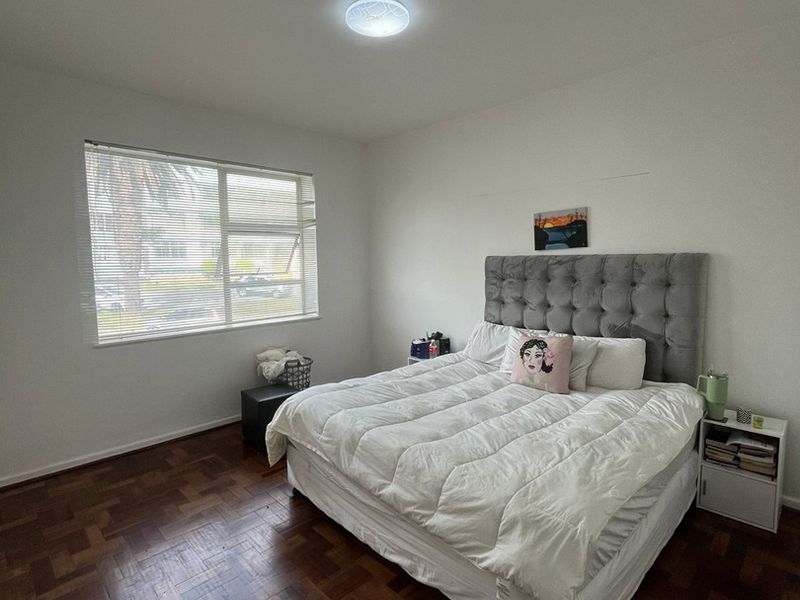 A well-lit bedroom featuring classic parquet flooring and a large window, providing a neutral foundation for personal styling.