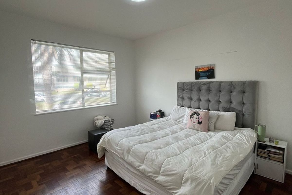 A well-lit bedroom featuring classic parquet flooring and a large window, providing a neutral foundation for personal styling.