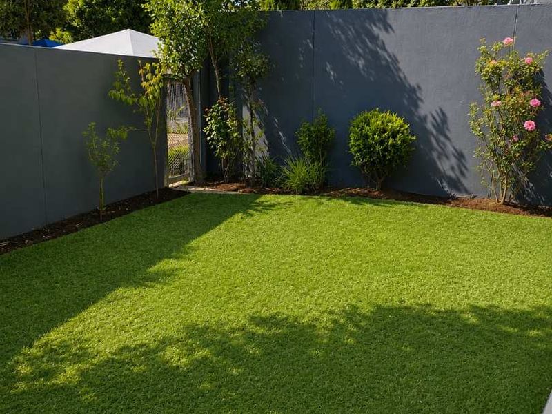 A well-maintained private rear garden featuring artificial turf, established landscaping, and a secure boundary wall with a pedestrian gate.
