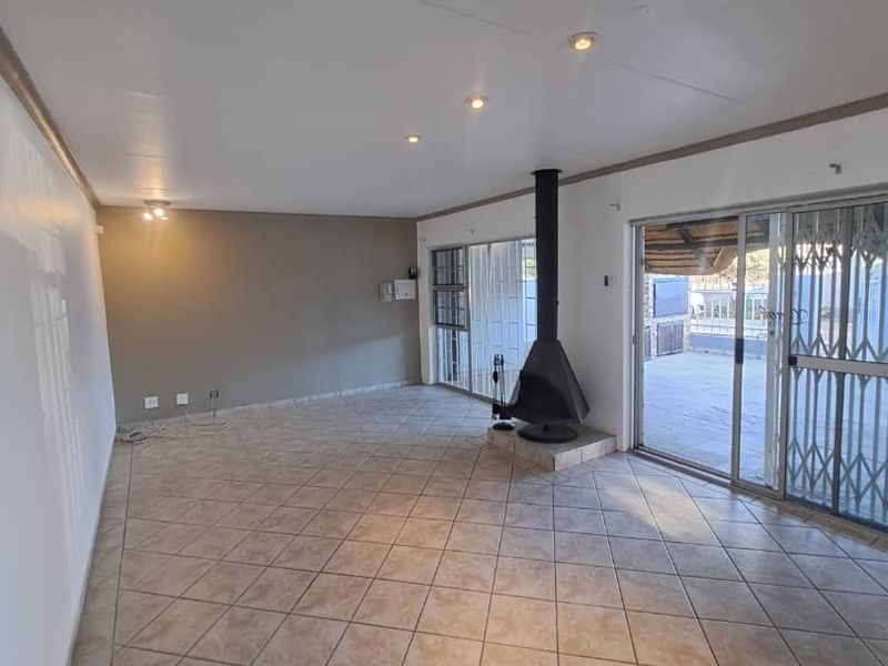 Spacious living area featuring neutral tiled flooring, a central freestanding fireplace, and large sliding glass doors providing access to the outdoor patio.