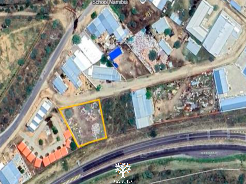 Aerial view of a vacant commercial land plot highlighted in yellow, situated in a developed area near a school and main road.