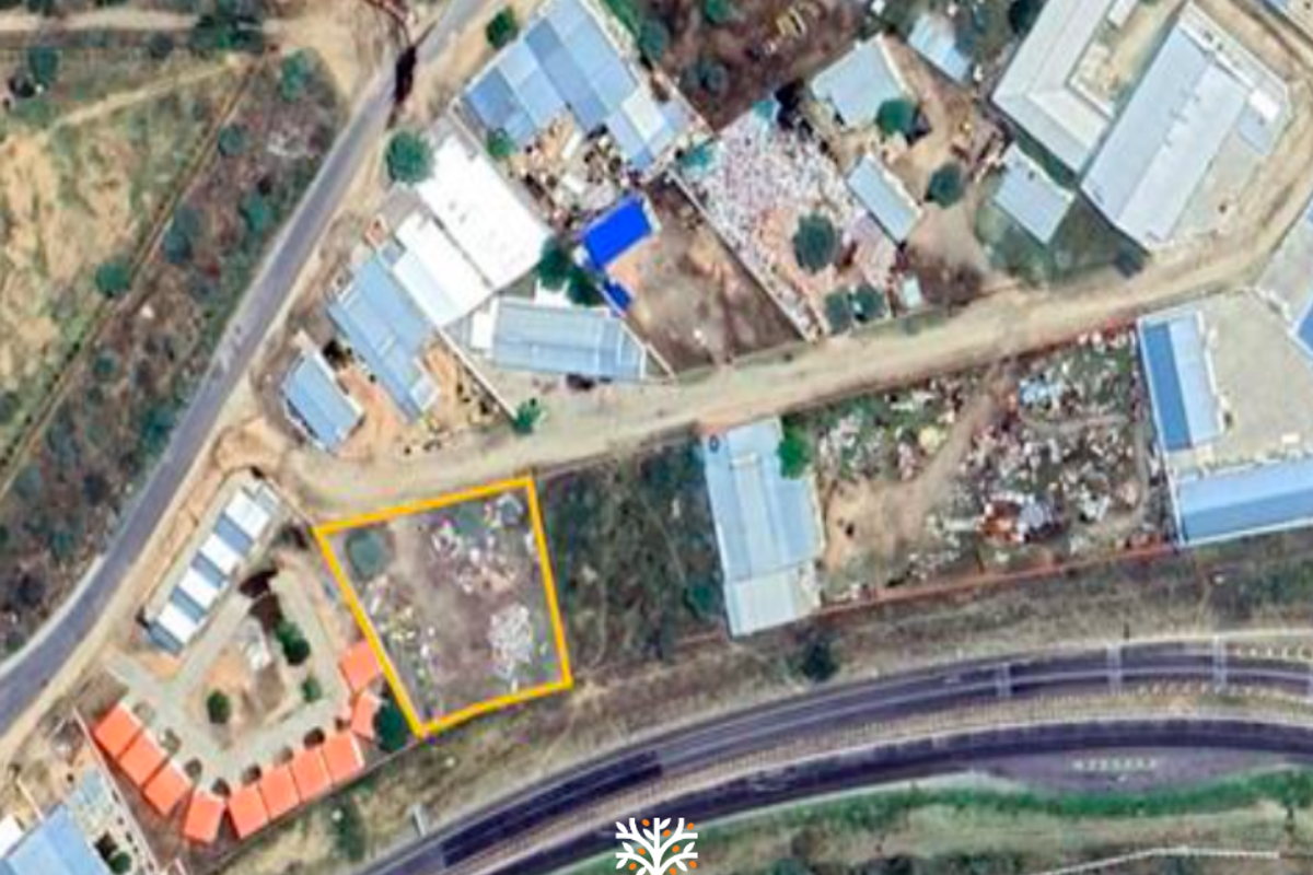 Aerial view of a vacant commercial land plot highlighted in yellow, situated in a developed area near a school and main road.
