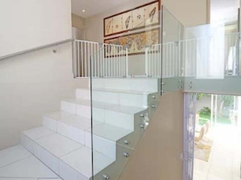 A bright hallway featuring a modern tiled staircase with a sleek glass balustrade and stainless steel handrail, leading to an open living area.
