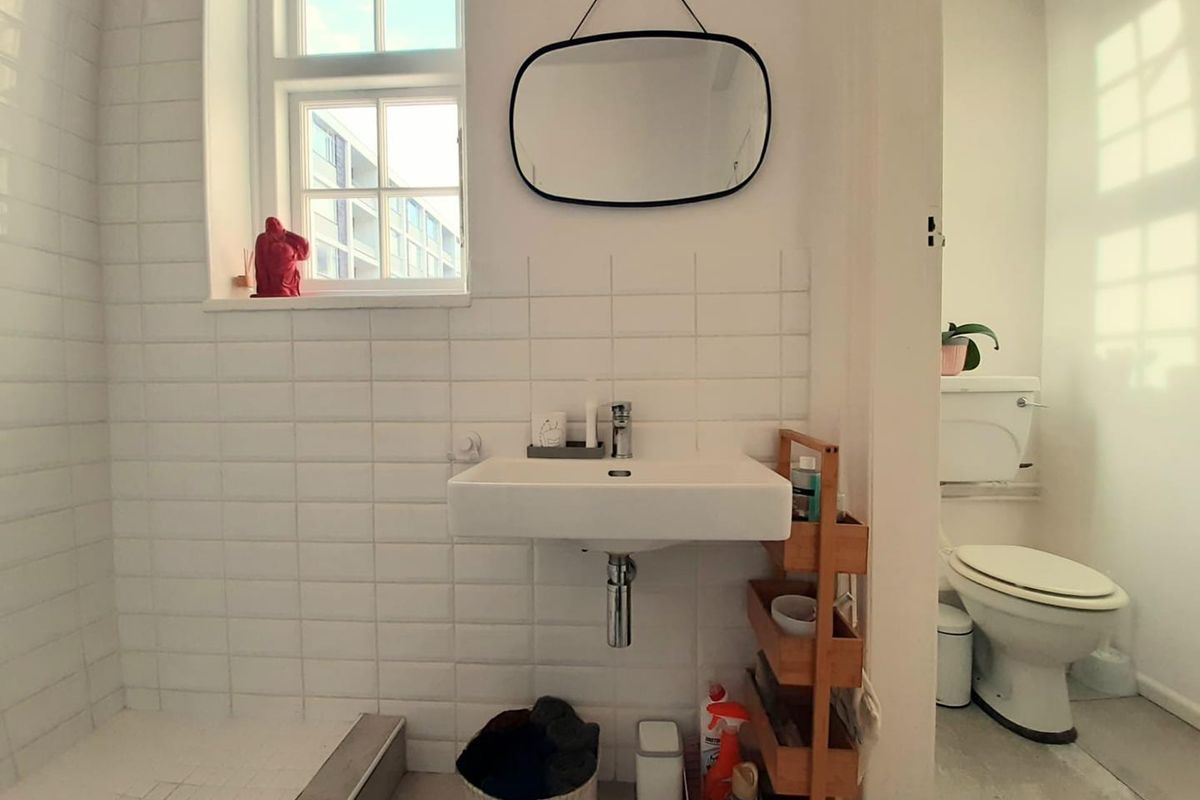 A bright bathroom featuring a wall-mounted basin, subway tile splashback, and a separate toilet area with natural light from the window.