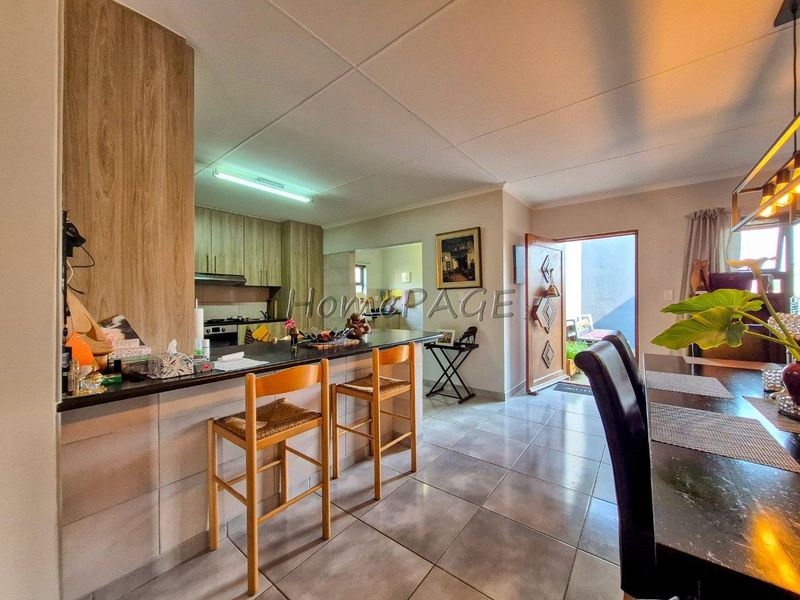 Open-plan living and kitchen area featuring a breakfast bar, modern cabinetry, built-in appliances, and tiled flooring with direct access to the exterior.