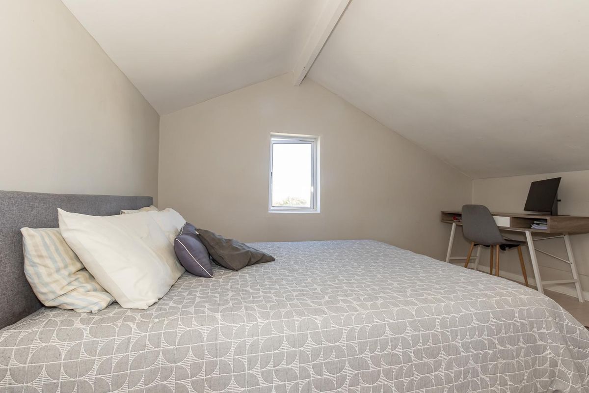 A cozy bedroom featuring a vaulted ceiling and a small window, providing a bright and functional space.