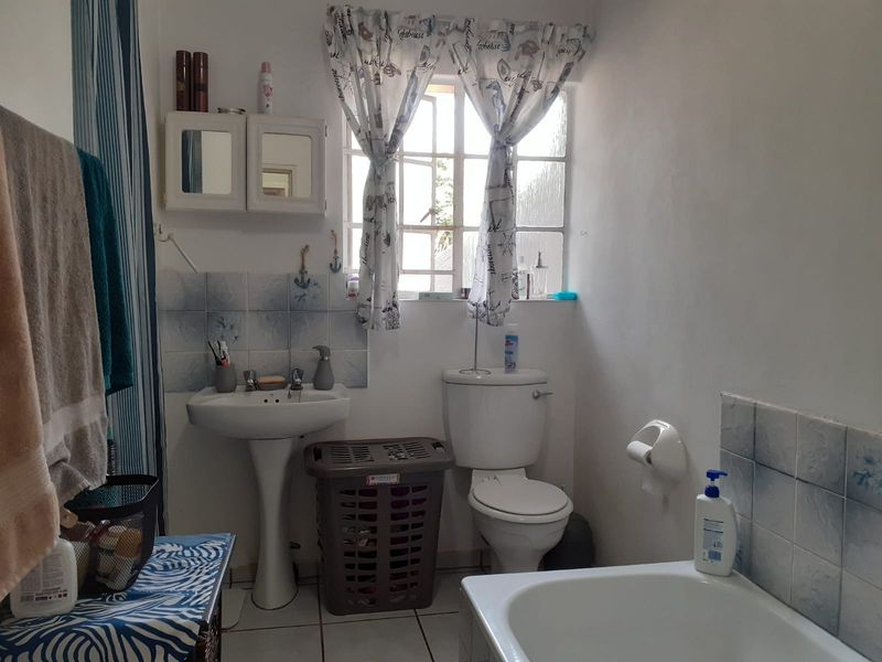 A functional bathroom featuring a pedestal basin, toilet, and bathtub with tiled splashbacks and flooring, offering potential for modernization and cosmetic updates.