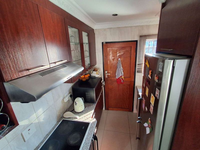A functional kitchen featuring dark wood cabinetry, an electric hob with an extractor fan, tiled backsplash, and tiled flooring.