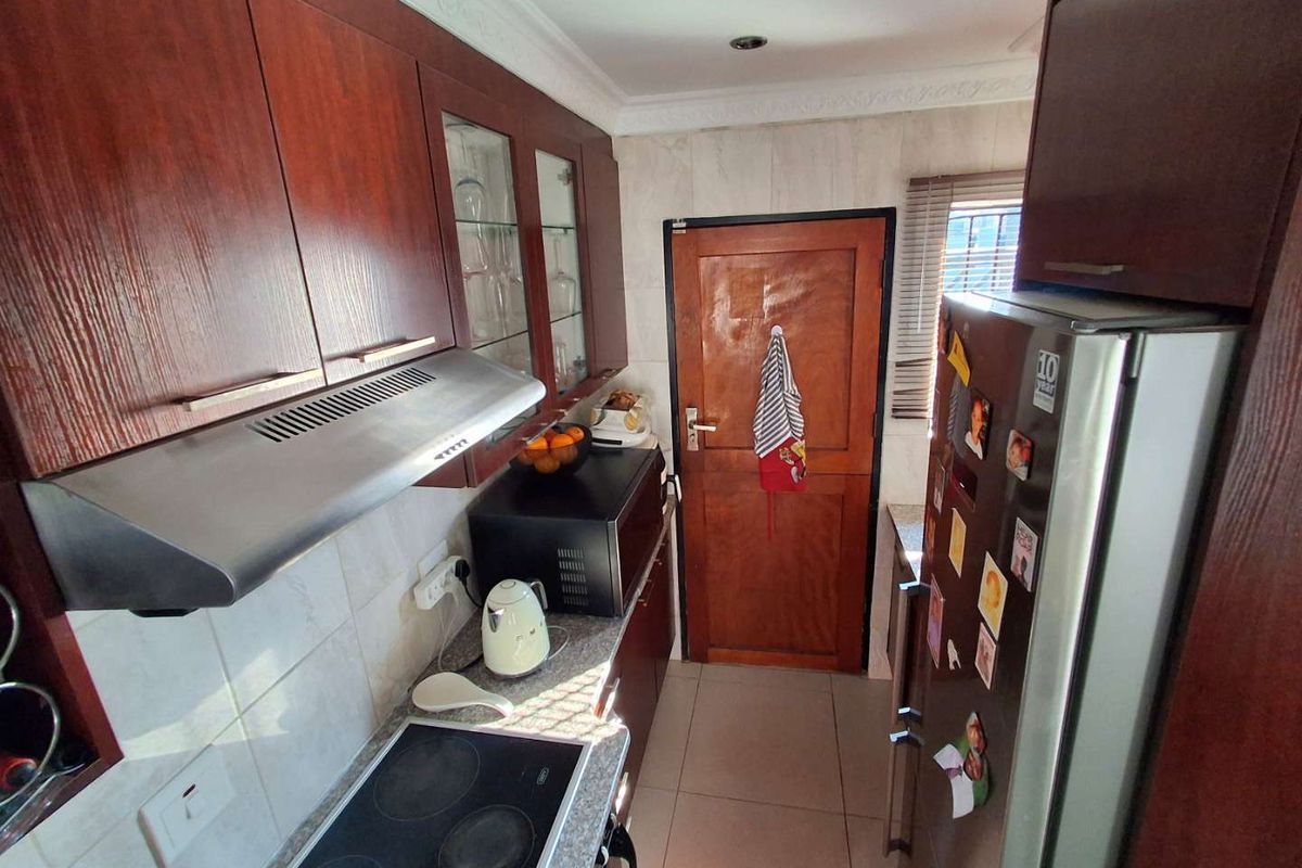 A functional kitchen featuring dark wood cabinetry, an electric hob with an extractor fan, tiled backsplash, and tiled flooring.