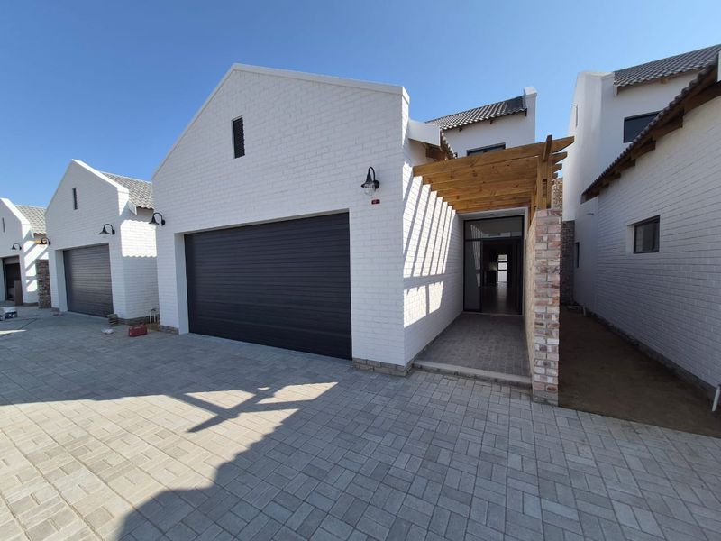 Modern townhouse exterior featuring a white brick facade, double garage, and a timber pergola over the entrance walkway with paved driveway.