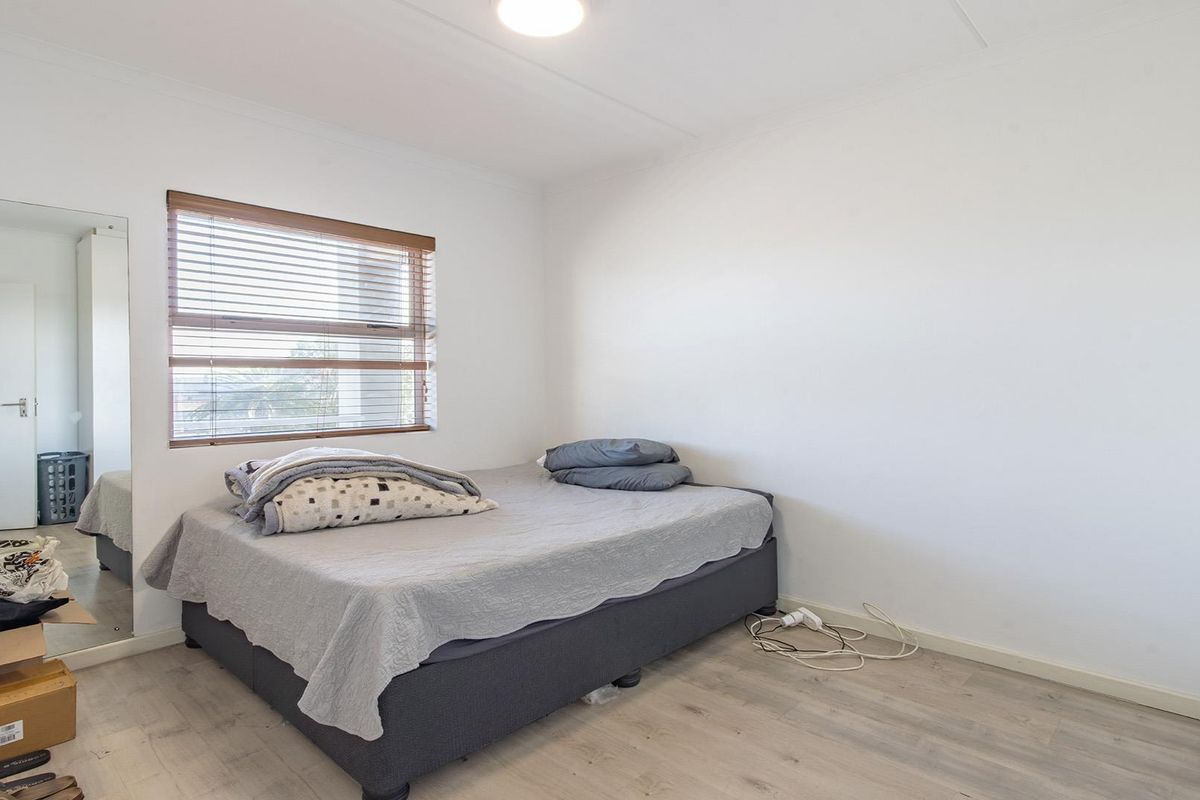 A functional bedroom featuring light-toned laminate flooring, a built-in wardrobe, and a window fitted with venetian blinds.