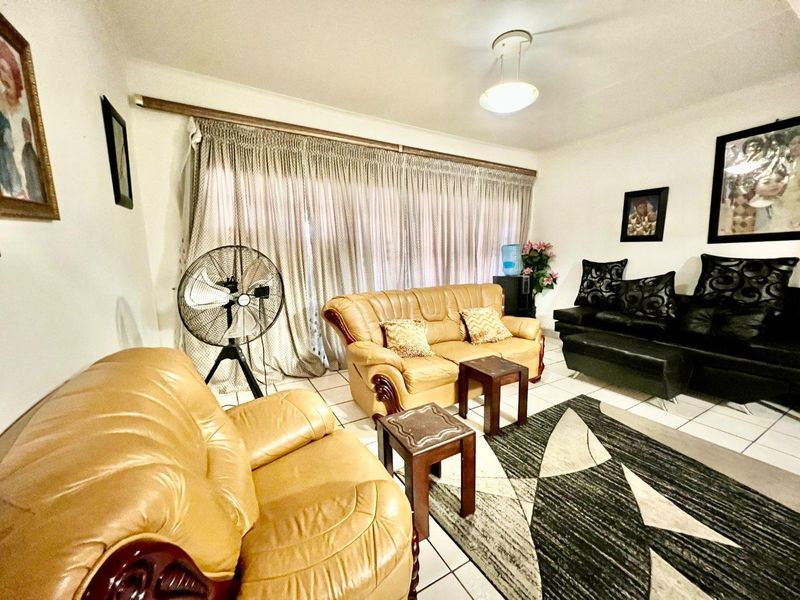 A living room featuring tiled flooring and a large window covered by curtains, providing a functional and neutral space for relaxation.