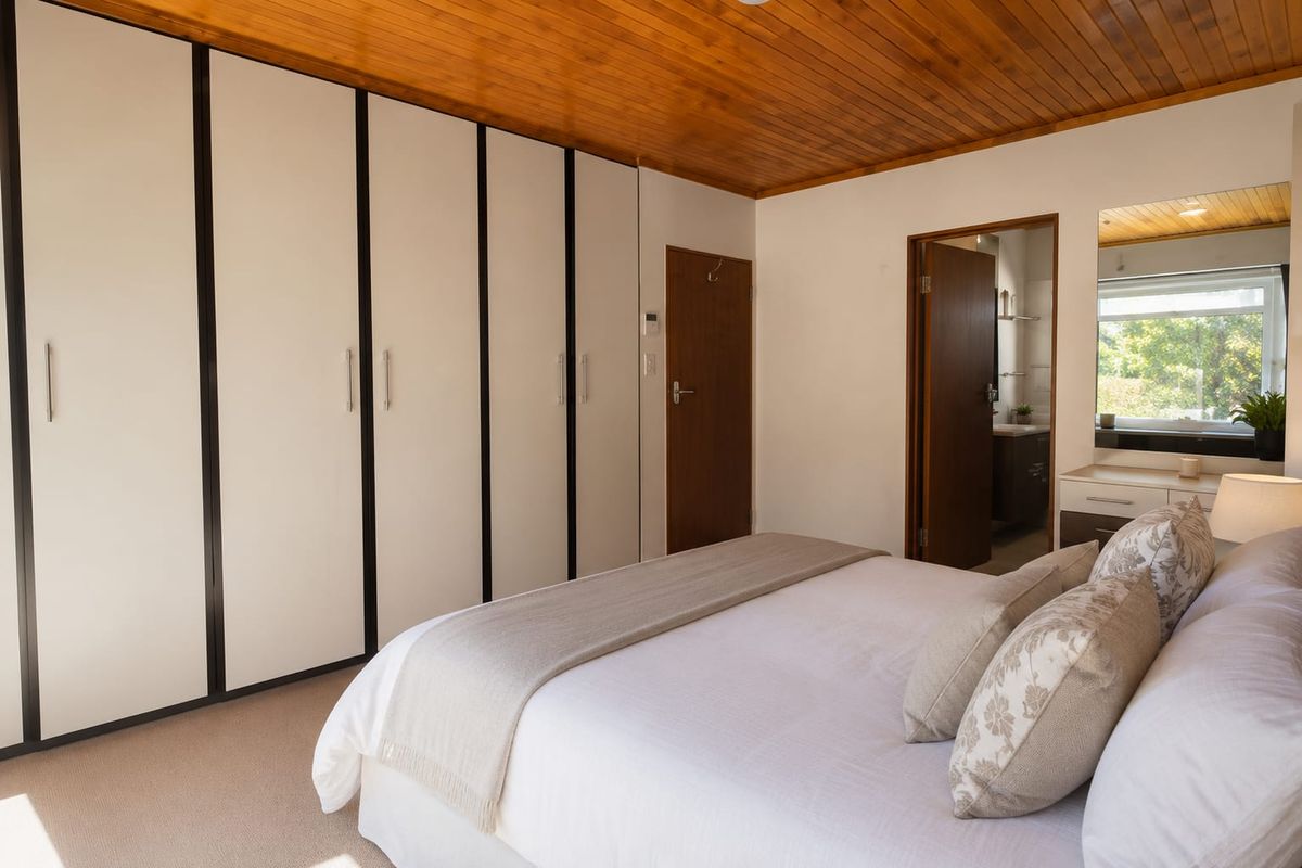 A well-maintained bedroom featuring built-in floor-to-ceiling wardrobes, a timber-paneled ceiling, and an en-suite bathroom access.