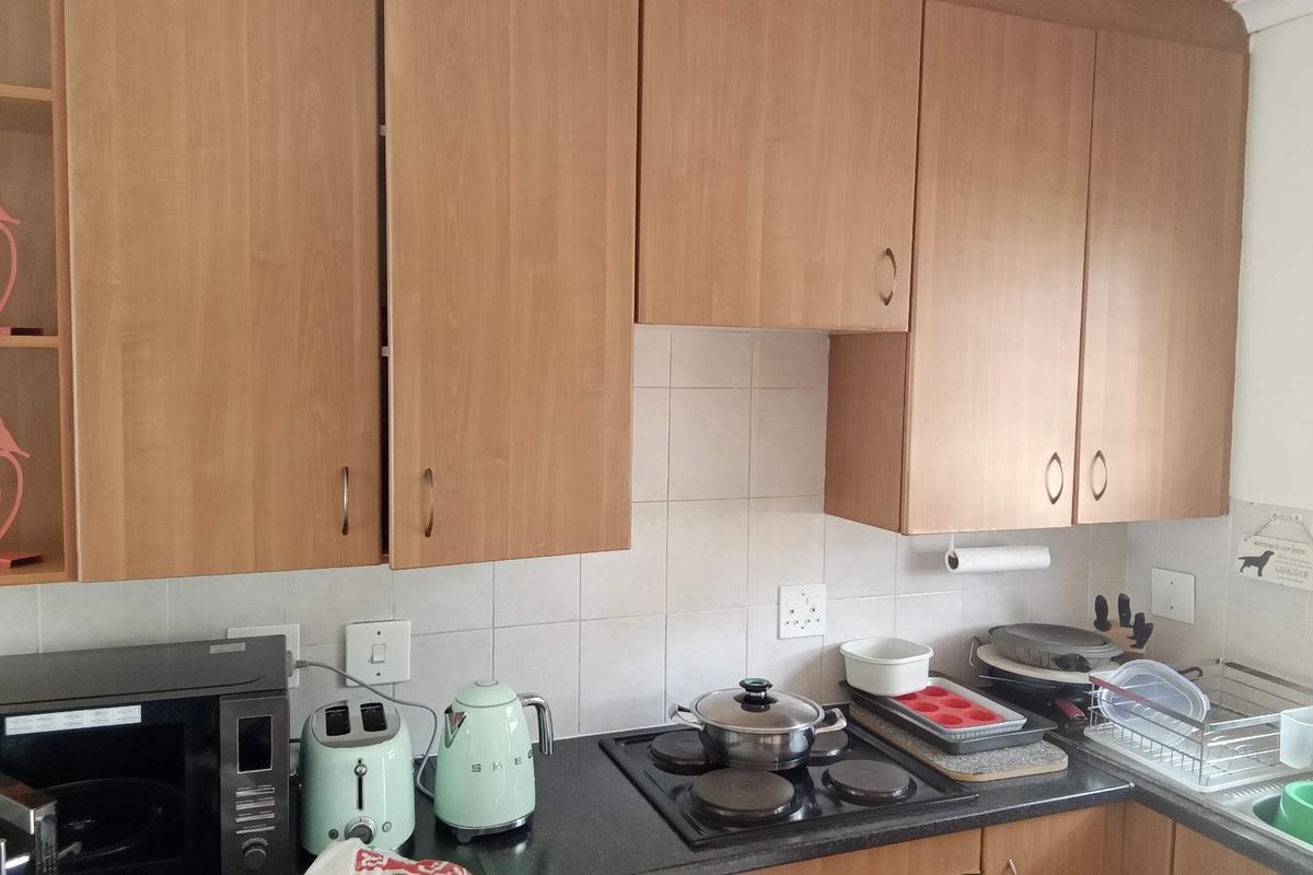 A functional kitchen area featuring light wood-finish cabinetry, a dark countertop, and a built-in electric hob with tiled splashback.