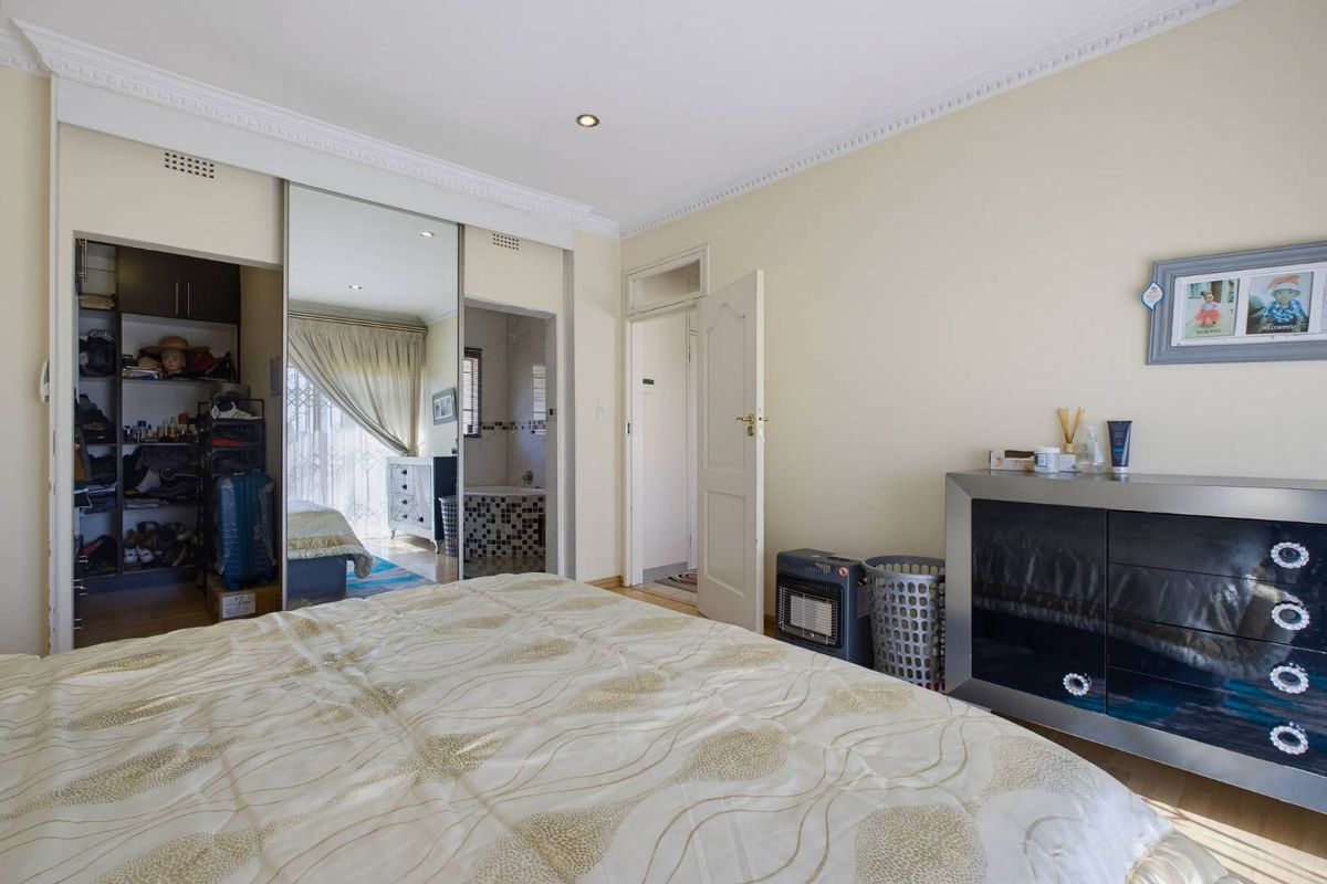 Spacious bedroom featuring built-in cupboards with mirrored sliding doors, recessed downlighting, and decorative ceiling cornicing.