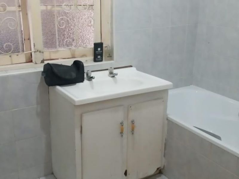A functional bathroom featuring a built-in vanity with basin, a standard bathtub, and tiled wall finishes, requiring some cosmetic updates to the cabinetry and window.
