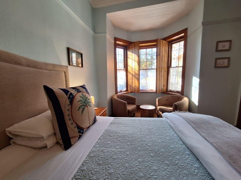 A cozy bedroom featuring a classic bay window with wooden shutters, crown molding, and traditional picture rails, providing a bright and inviting atmosphere.