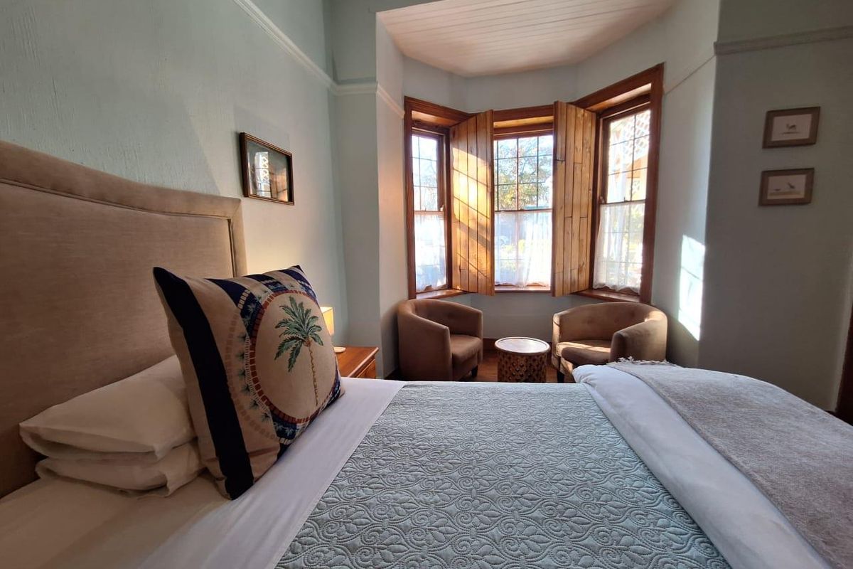 A cozy bedroom featuring a classic bay window with wooden shutters, crown molding, and traditional picture rails, providing a bright and inviting atmosphere.