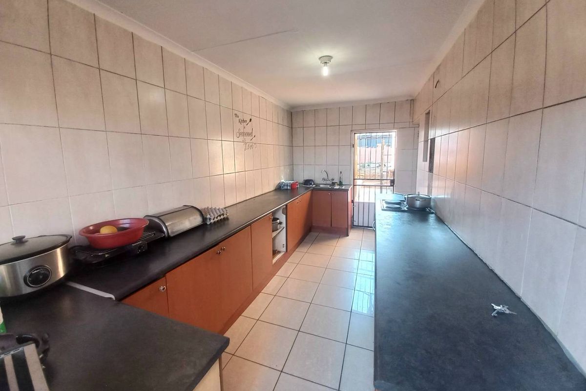 A functional galley-style kitchen featuring extensive laminate countertops, wooden cabinetry, and full-height wall tiling with direct access to the exterior.