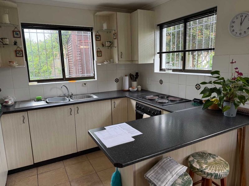 A functional kitchen featuring laminate cabinetry, dark countertops, a double sink, and an integrated electric hob and oven with tiled backsplash.