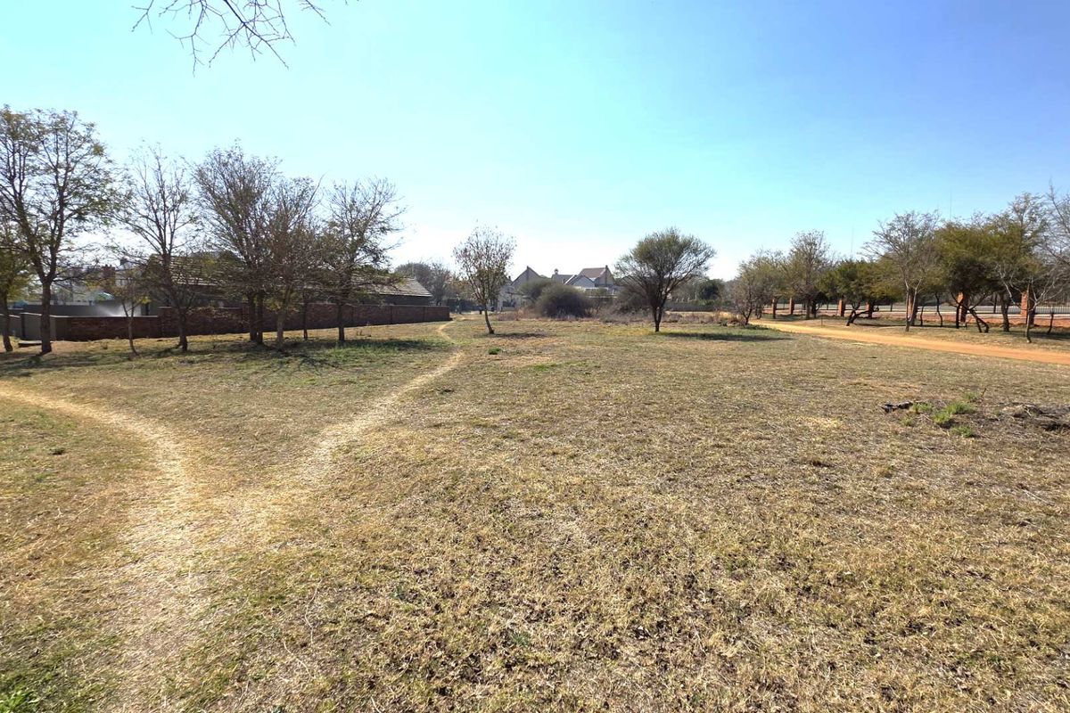 A wide-angle view of a vacant residential plot featuring established trees, natural grass, and a perimeter brick wall.