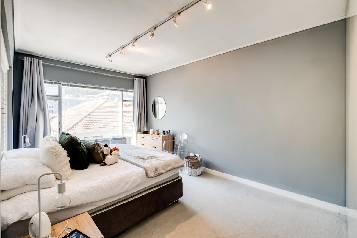 A well-lit bedroom featuring neutral grey walls, carpeted flooring, and large windows that provide natural light and an exterior view.