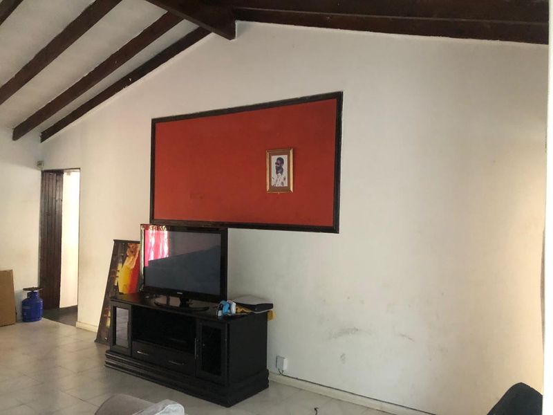 Living room featuring exposed timber ceiling beams and tiled flooring, with visible wall scuffing and wear requiring cosmetic attention.