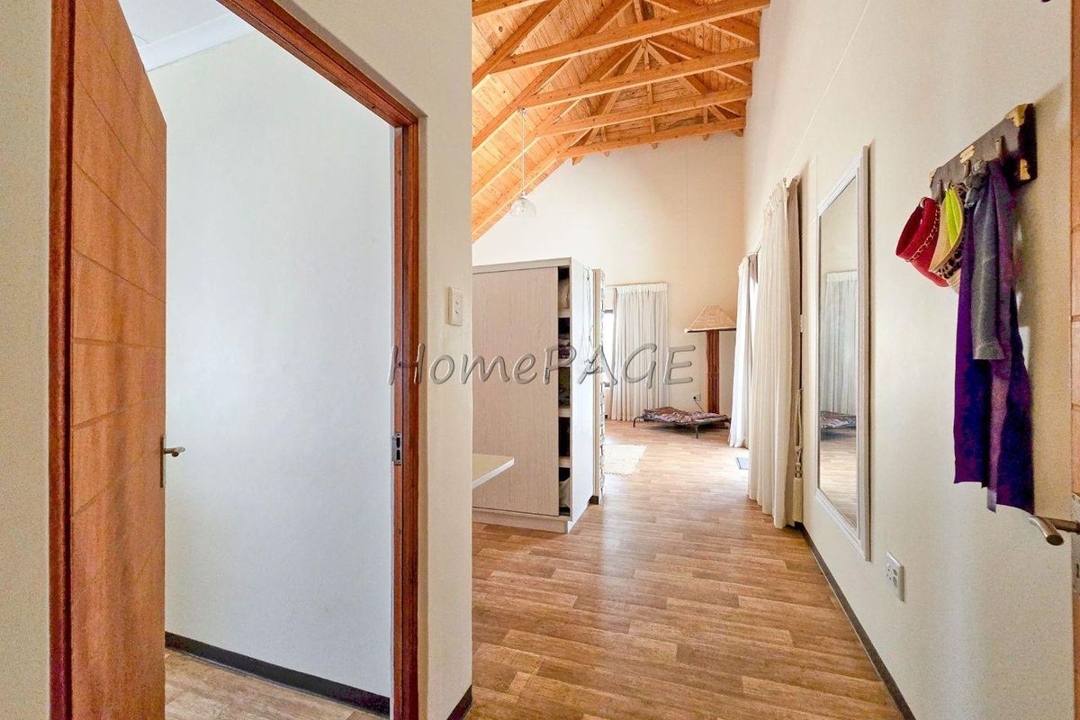 Spacious bedroom featuring high vaulted timber ceilings, wood-look flooring, and an open-plan layout with direct access to an adjoining room.