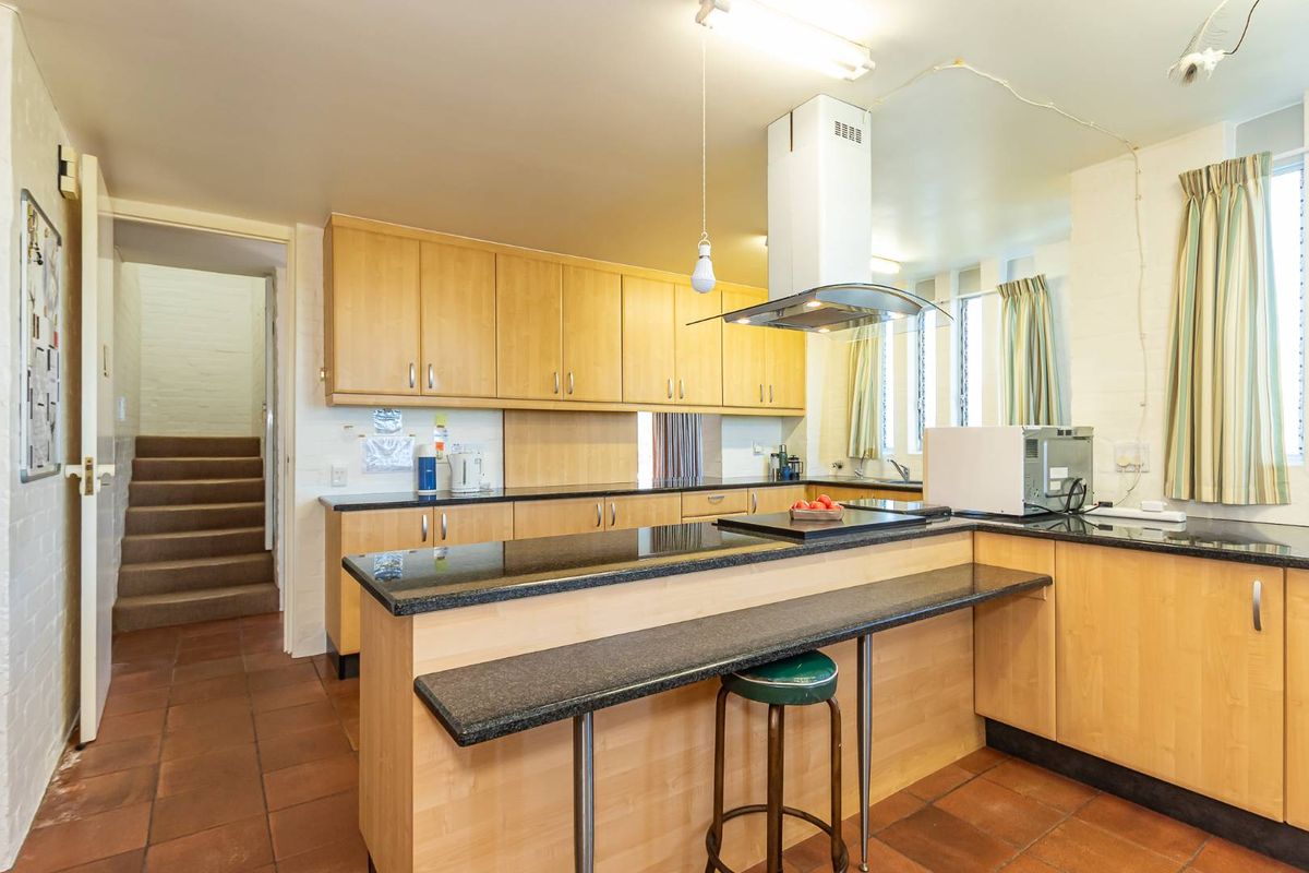 Functional kitchen featuring light wood cabinetry, dark granite countertops, a breakfast bar, and a stainless steel extractor fan.