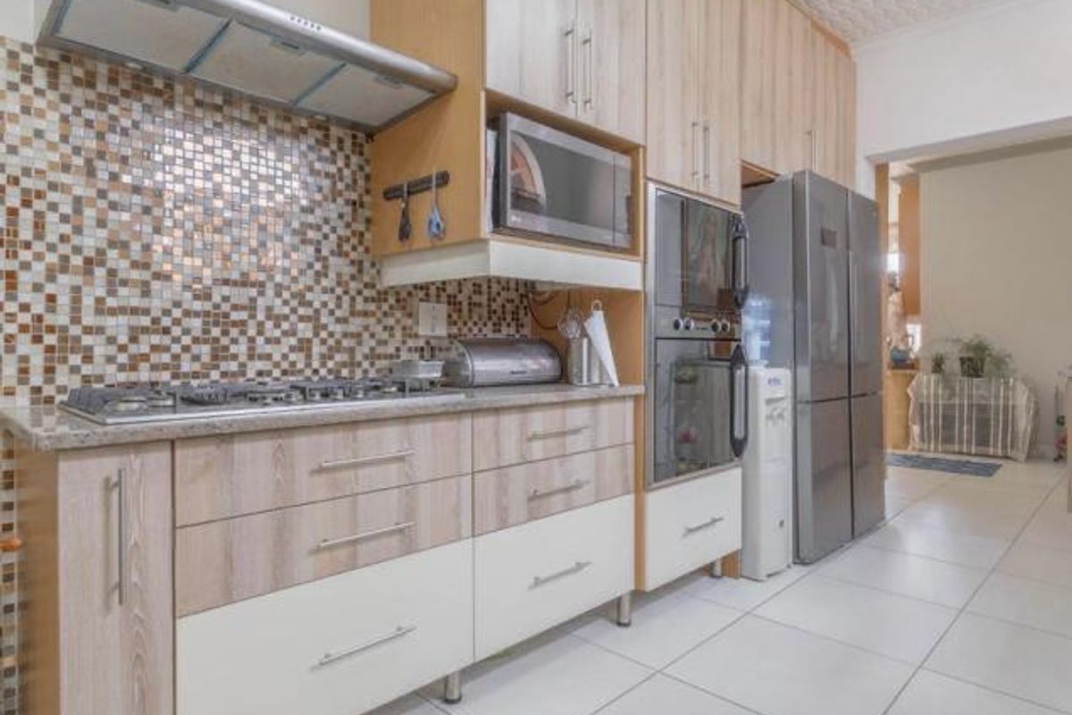 Modern kitchen featuring light wood-tone cabinetry, mosaic tile backsplash, built-in oven, gas hob, and stainless steel extractor fan with tiled flooring.