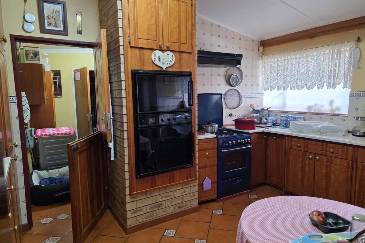 A traditional kitchen featuring wooden cabinetry, a built-in oven, a gas stove, and tiled flooring, with an adjacent doorway leading to a utility area.