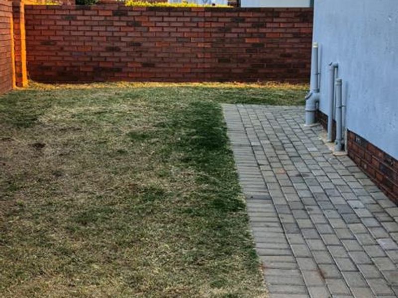 A private rear garden area featuring a paved walkway, lawn, and brick boundary wall, providing a functional outdoor space for the apartment.