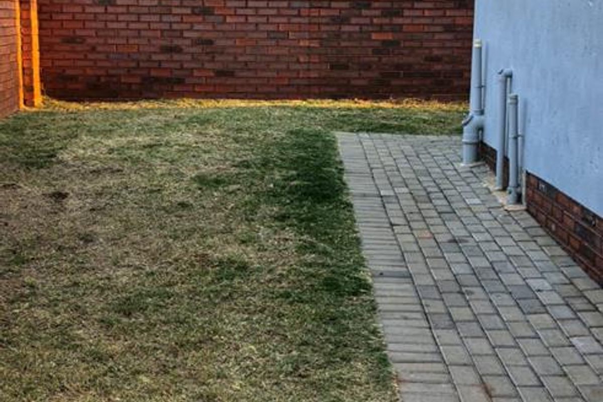A private rear garden area featuring a paved walkway, lawn, and brick boundary wall, providing a functional outdoor space for the apartment.