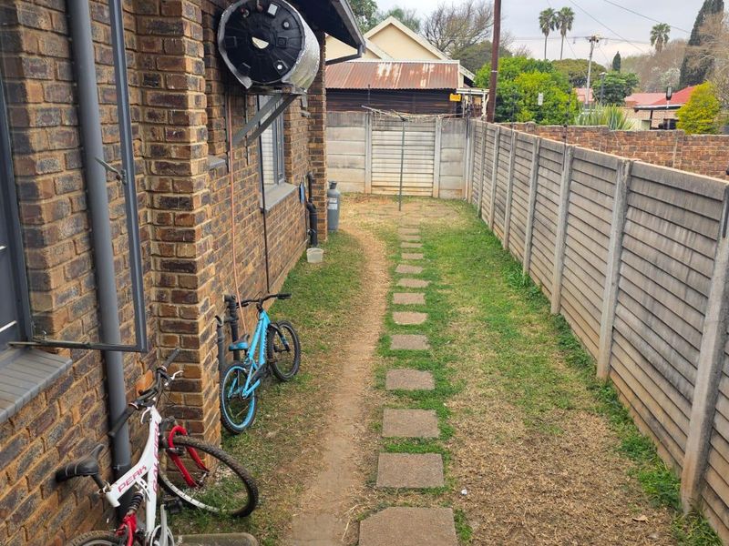 A narrow rear garden area featuring a brick exterior wall, solar geyser, precast concrete boundary fencing, and a stepping stone pathway.