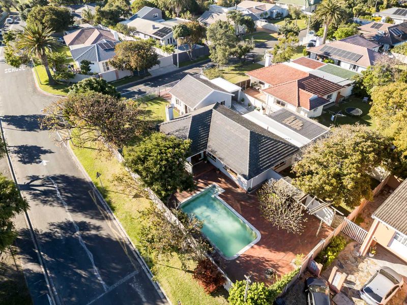 Aerial view of a residential property featuring a swimming pool, paved patio area, and tiled roof, situated in a suburban neighborhood.