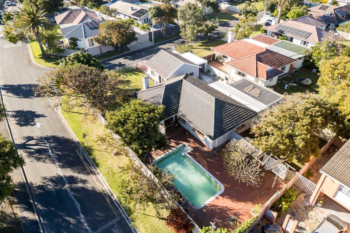 Aerial view of a residential property featuring a swimming pool, paved patio area, and tiled roof, situated in a suburban neighborhood.