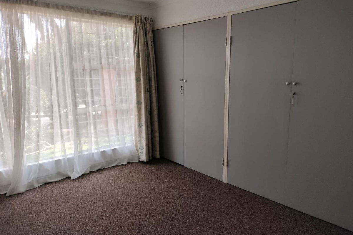 A bedroom featuring built-in cupboards and large windows with natural light, finished with carpeted flooring.