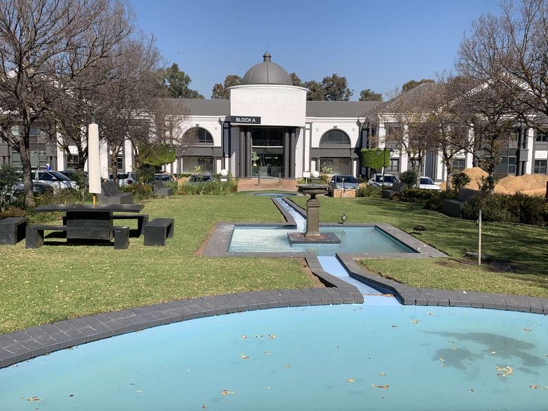 A well-maintained office park exterior featuring a central water fountain, landscaped gardens, and a prominent building entrance with a domed architectural design.