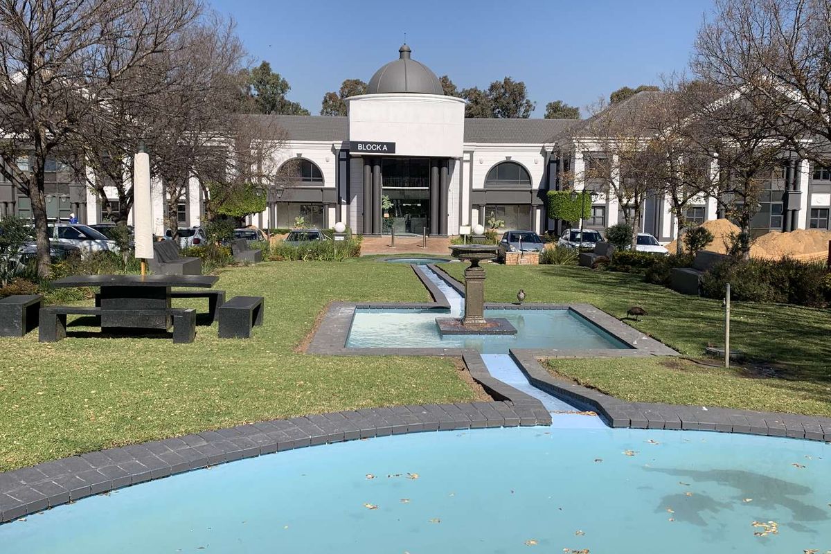 A well-maintained office park exterior featuring a central water fountain, landscaped gardens, and a prominent building entrance with a domed architectural design.