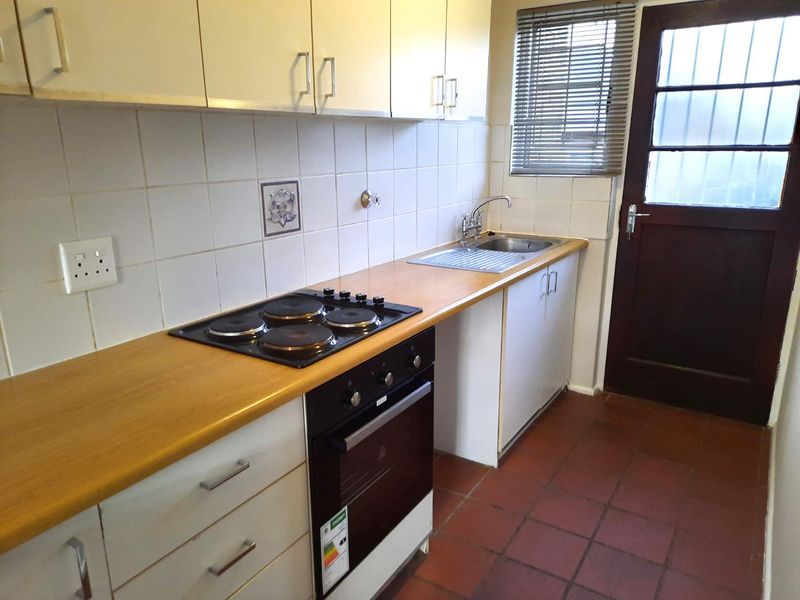 A functional, compact kitchen featuring built-in cabinetry, an electric hob, oven, and direct access to the exterior via a rear door.
