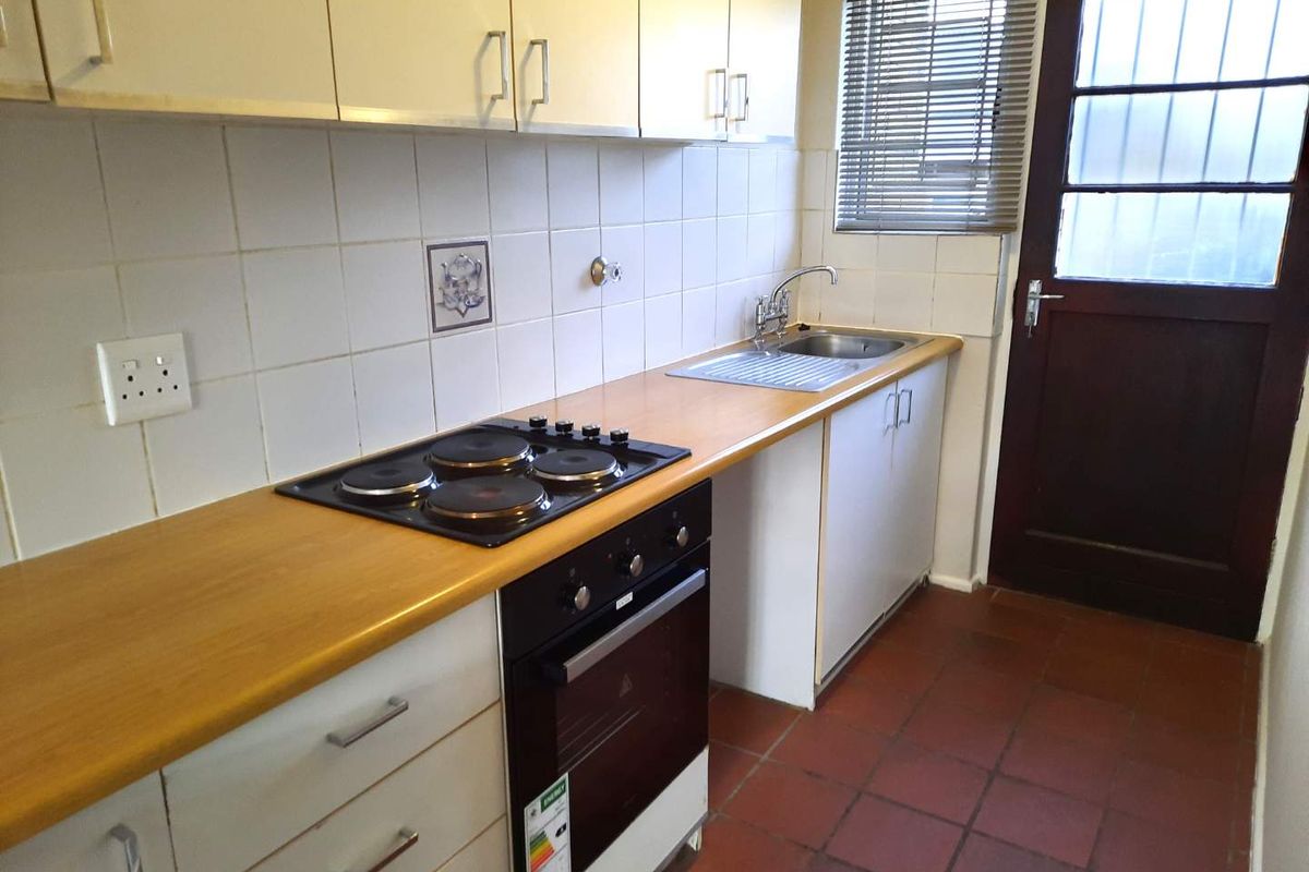 A functional, compact kitchen featuring built-in cabinetry, an electric hob, oven, and direct access to the exterior via a rear door.