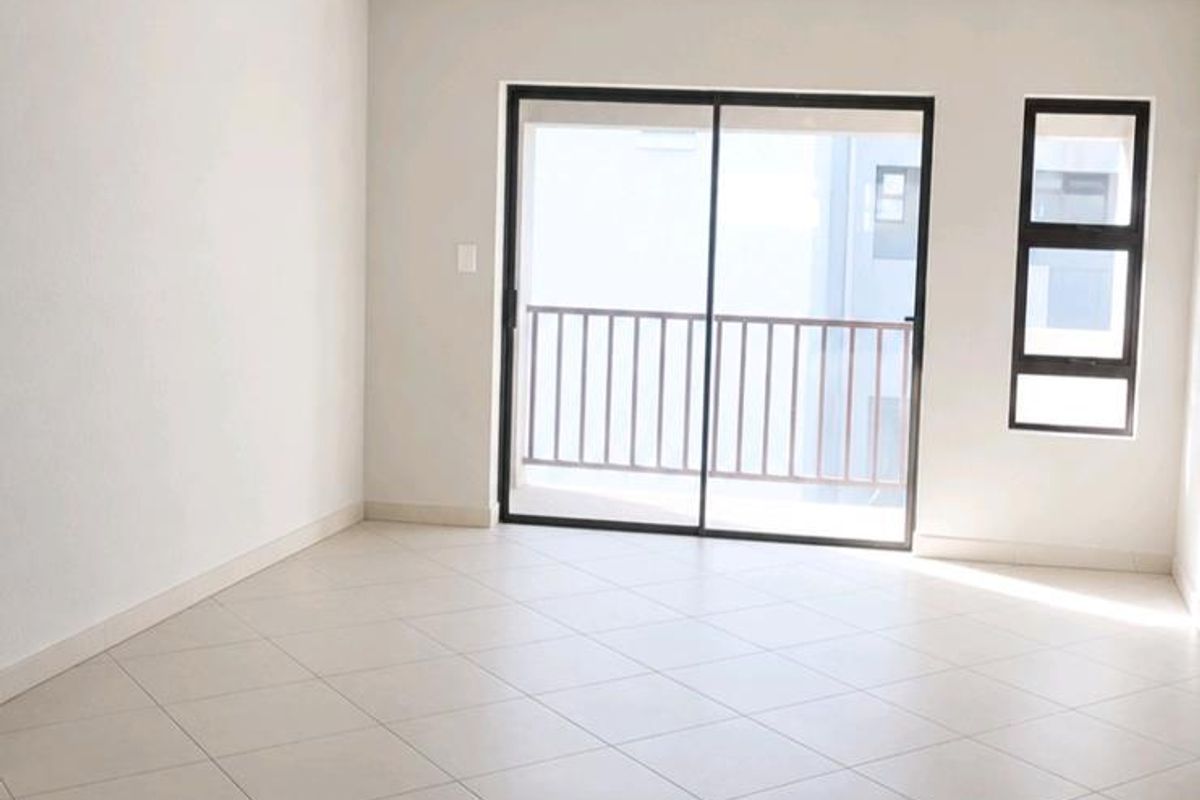 A bright, empty living room featuring neutral tiled flooring, a sliding glass door leading to a balcony, and clean, modern finishes.