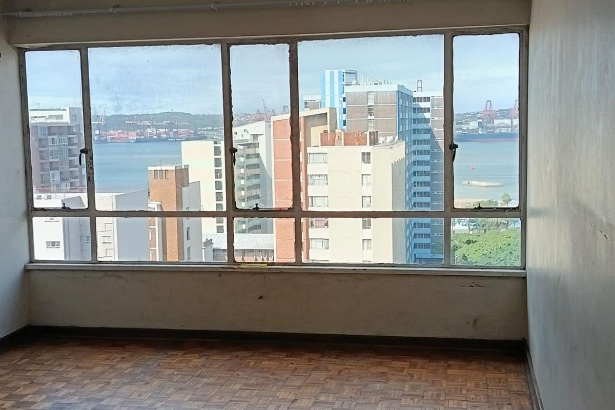 An empty living room featuring original parquet flooring and large windows offering expansive urban and harbour views.