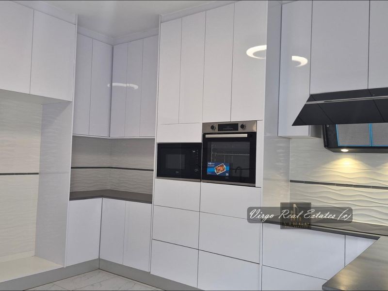 Modern kitchen featuring high-gloss white cabinetry, integrated appliances including an oven and microwave, and a stylish textured tile backsplash.