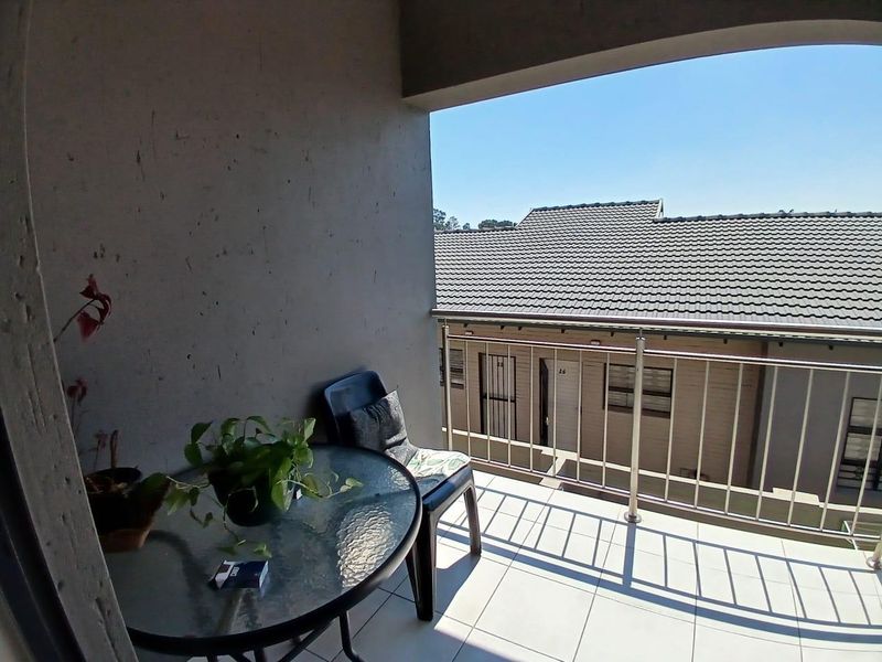 A covered balcony featuring tiled flooring and a stainless steel balustrade, offering an outdoor space with views of the surrounding complex.
