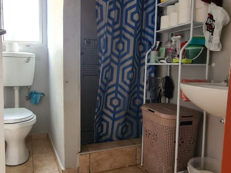 A functional bathroom featuring a pedestal basin, flush toilet, and a shower enclosure with tiled flooring and basic finishes.