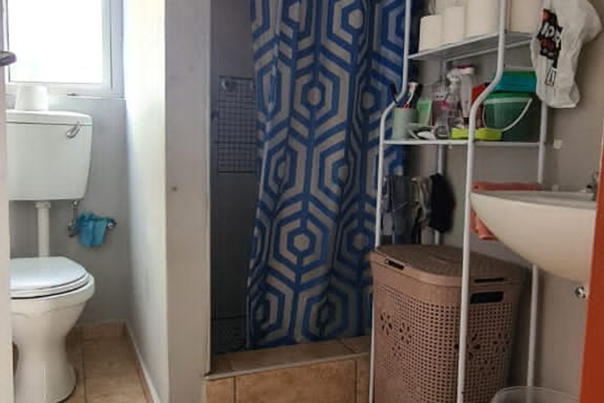 A functional bathroom featuring a pedestal basin, flush toilet, and a shower enclosure with tiled flooring and basic finishes.