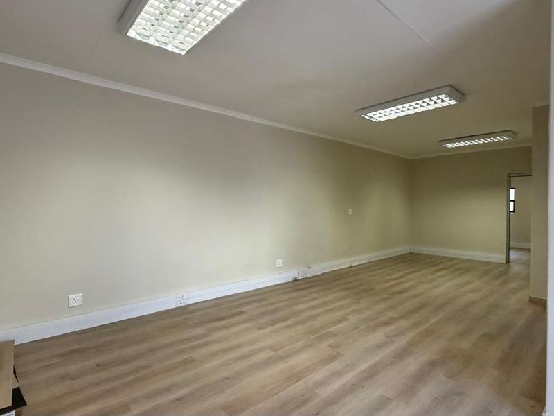 An empty, open-plan office space featuring laminate flooring and recessed fluorescent lighting, suitable for a professional workspace setup.