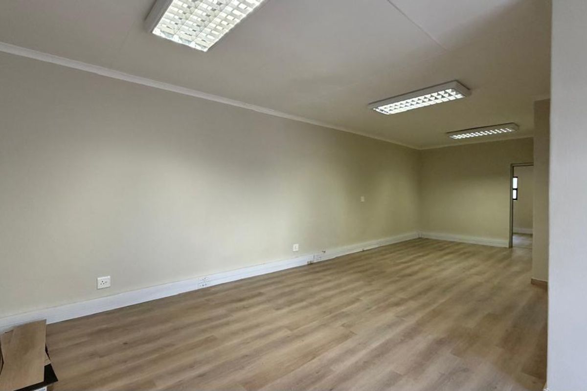 An empty, open-plan office space featuring laminate flooring and recessed fluorescent lighting, suitable for a professional workspace setup.