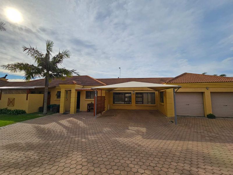 Front exterior view of a townhouse featuring a paved driveway, double garage, and a shade sail carport.